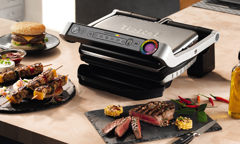Tefal GC702D Optigrill sw/geb. edelst. inkl. Hamburgerpresse. auf dem Tisch mit frisch gegrilltem Fleisch.